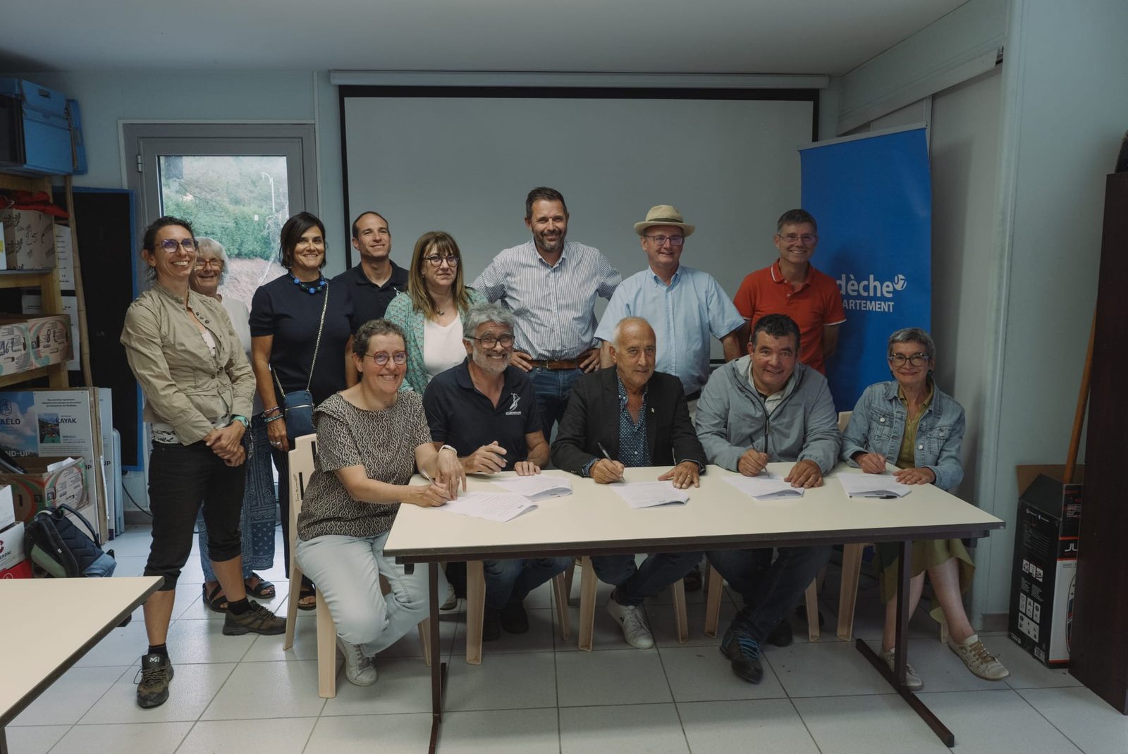 Signature de la convention d'organisation autour d'une table, dans les locaux du club Eyrieux Canoë-Kayak, entourée des élus et des représentants du canoë-kayak.